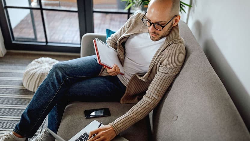 Man sitting on the couch with his laptop and notebook