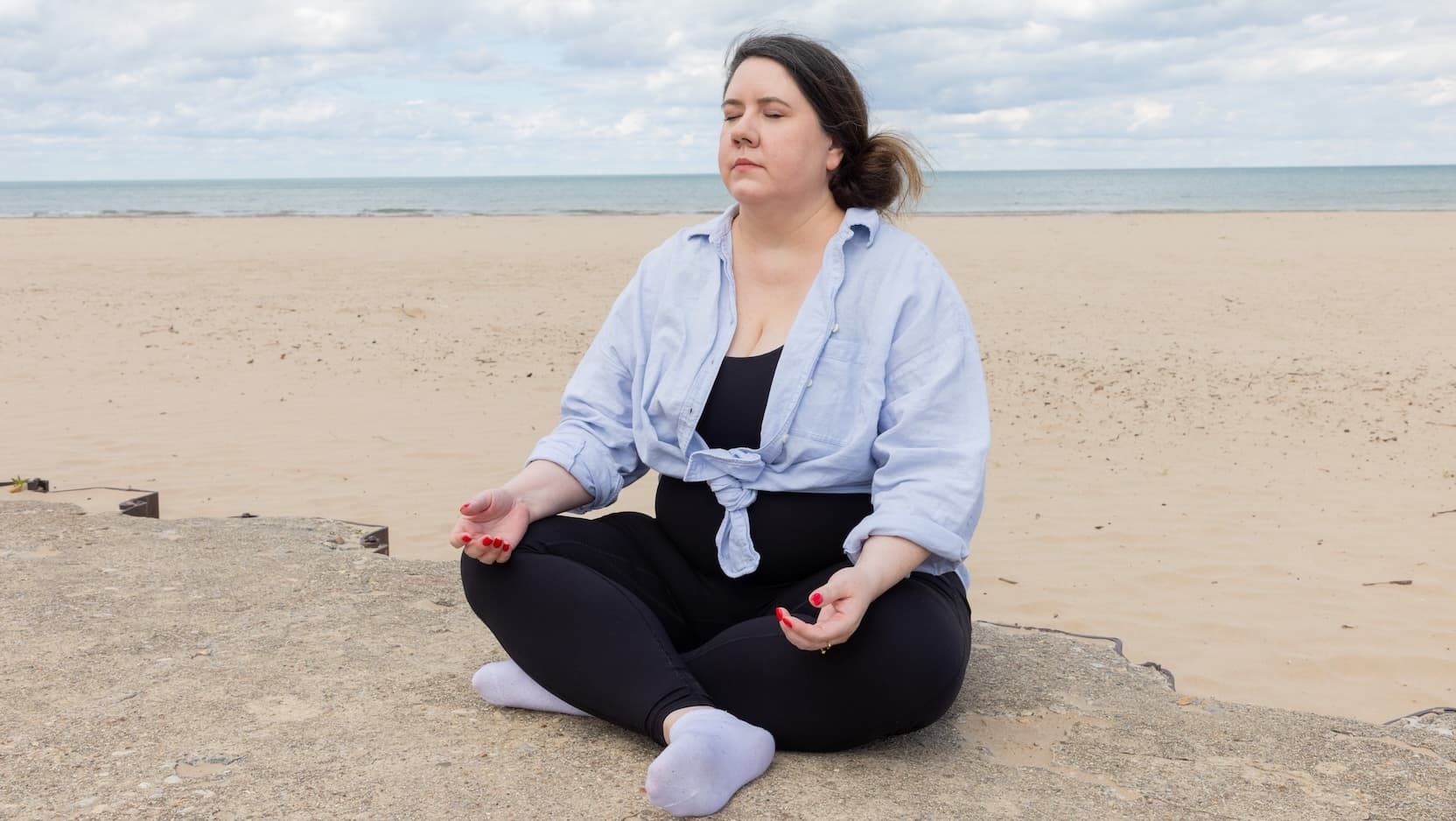 Shanna Quinn meditates cross legged on the beach