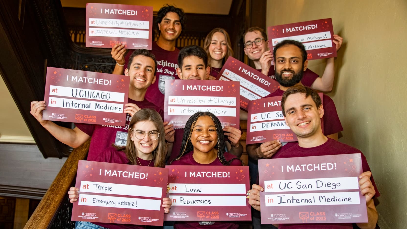 A diverse group of smiling med students hold up signs that say "I Matched!" followed by spaces in which each person's match location and specialty is handwritten.