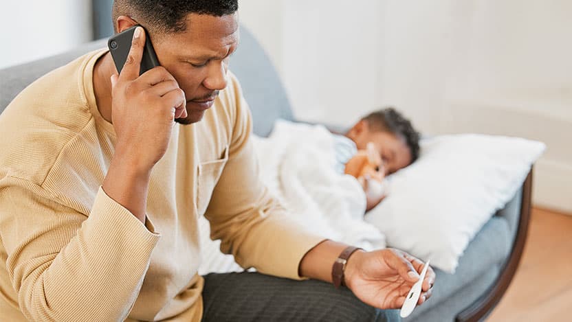 Dad with sick child, checking temperature and calling the pediatrician