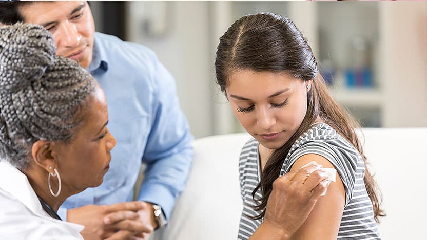 Father watching as doctor places bandage on teen's arm after giving a shot