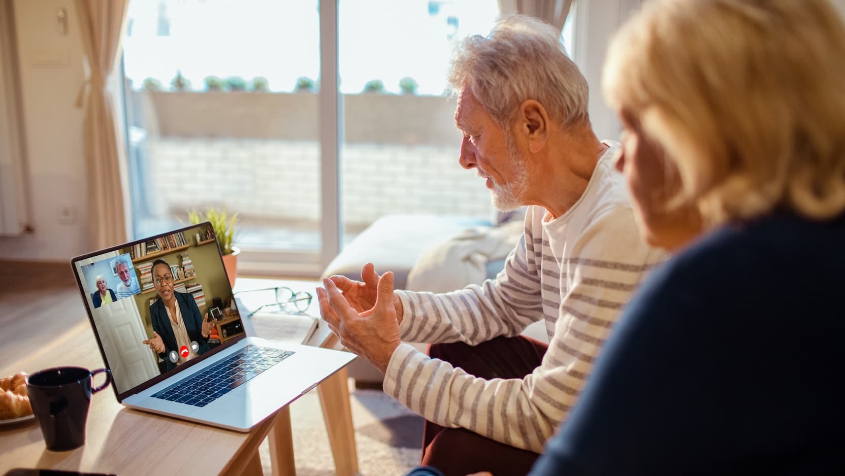 A senior couple speaks to a doctor via a telemedicine call on a laptop.