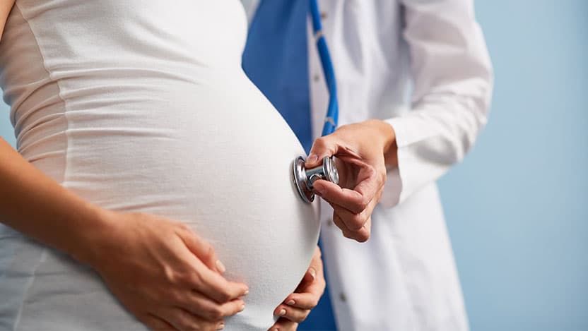 Doctor listening breath of baby in pregnant female abdomen