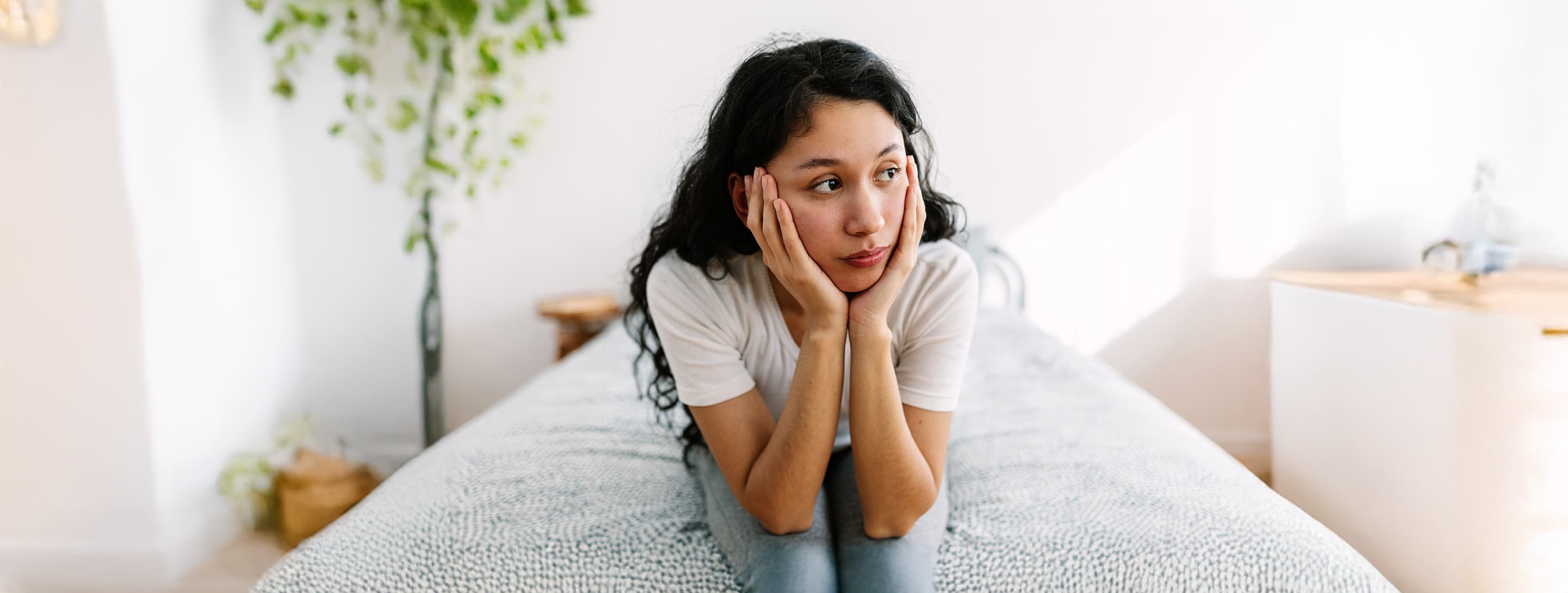 Young woman, sitting on bed, contemplating