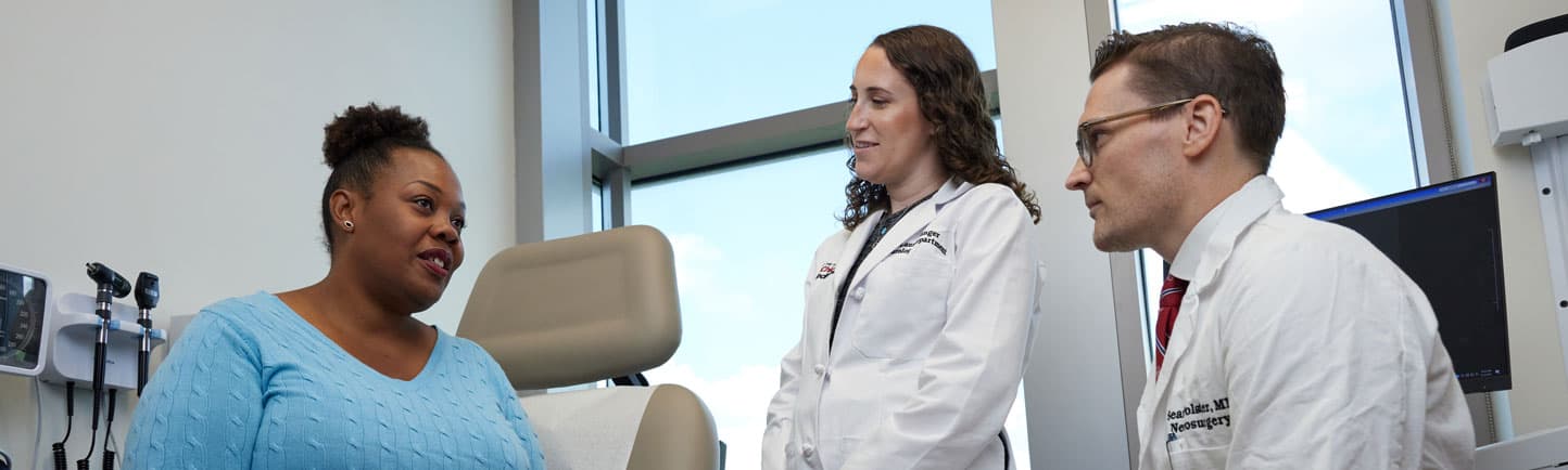 Lauren Singer, MD and Sean Polster, MD talking to a female patient in a clinic room.